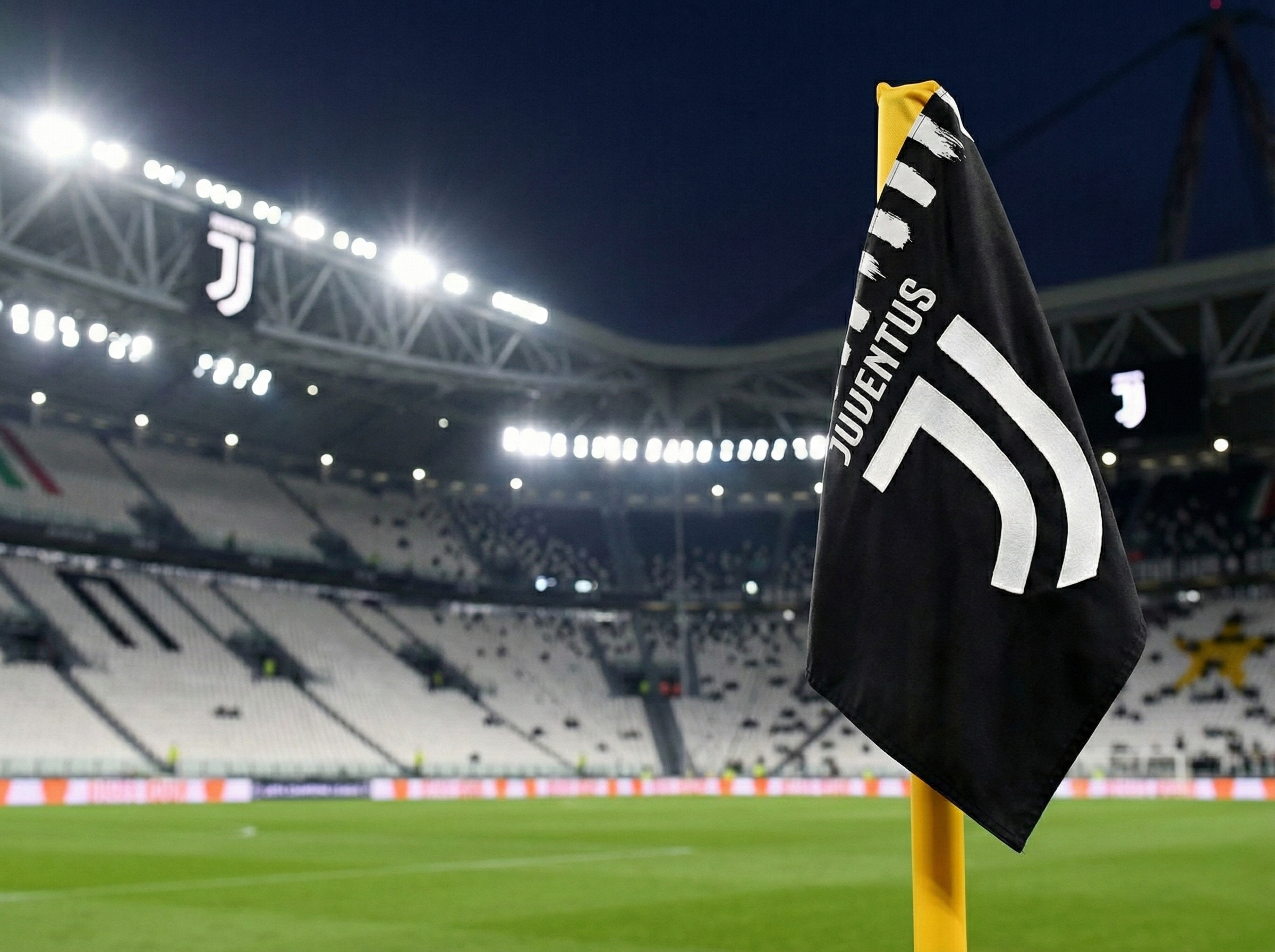 Die Eckfahne von Juventus mit dem modernen Logo im Juventus Stadium in Turin, aufgenommen bei Nacht. Die leeren Zuschauerränge im Hintergrund sind in den Vereinsfarben Schwarz und Weiß gehalten.
